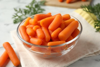 Photo of Baby carrots in bowl and leaves on white marble table