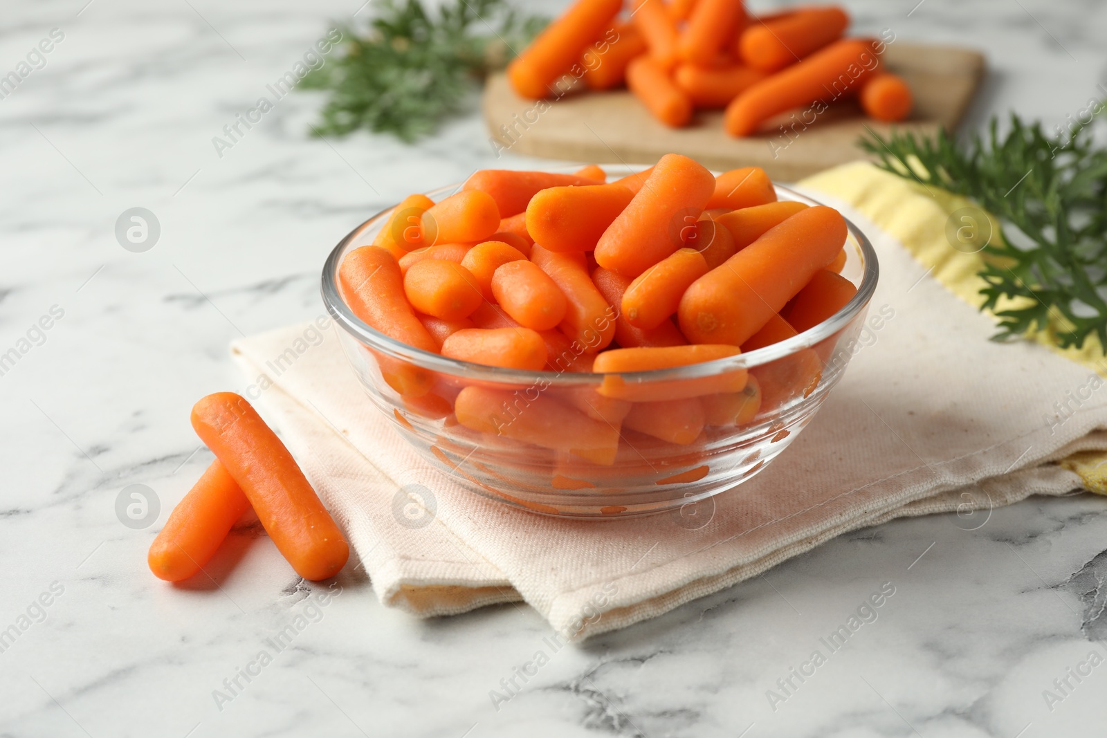 Photo of Baby carrots in bowl and green leaves on white marble table