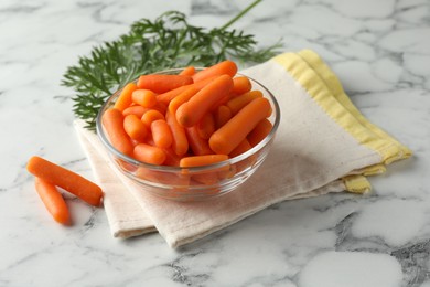 Baby carrots in bowl and green leaves on white marble table