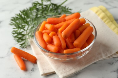 Baby carrots in bowl and green leaves on white marble table