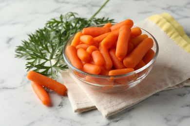 Photo of Baby carrots in bowl and green leaves on white marble table