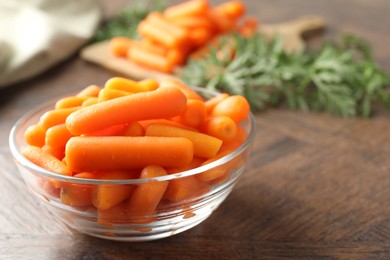 Photo of Baby carrots in bowl on wooden table, space for text