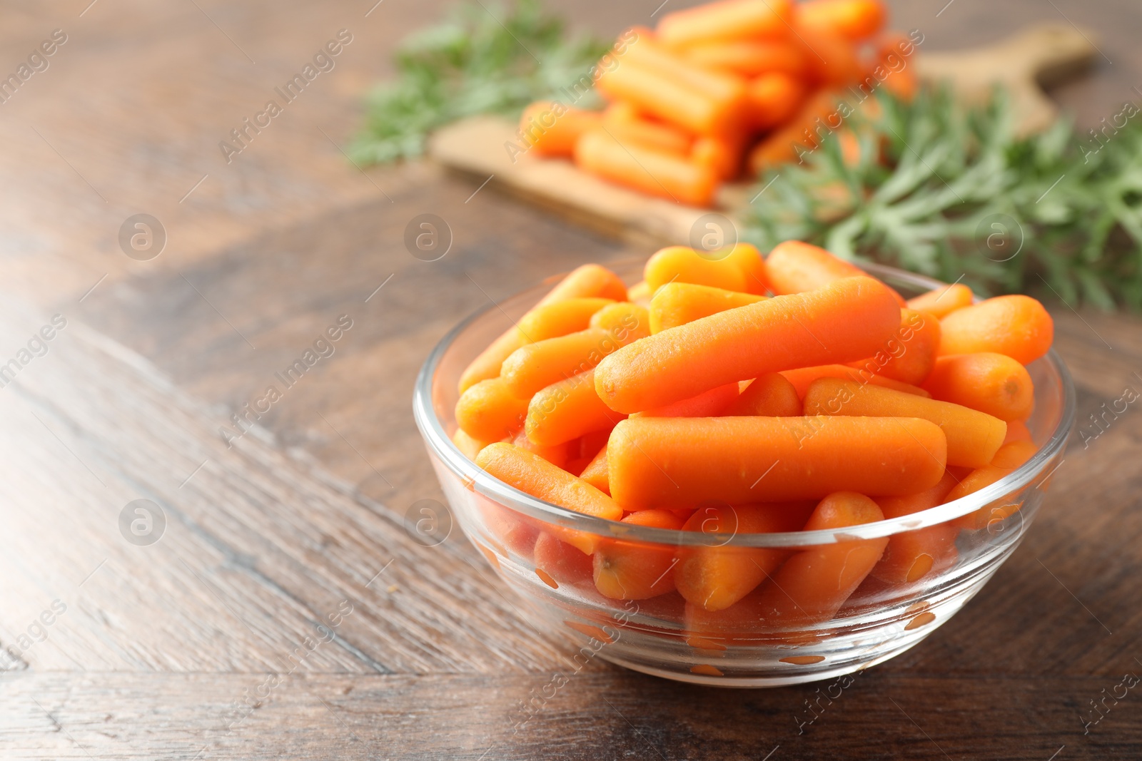 Photo of Baby carrots in bowl on wooden table, space for text