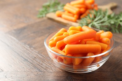 Baby carrots in bowl on wooden table, space for text