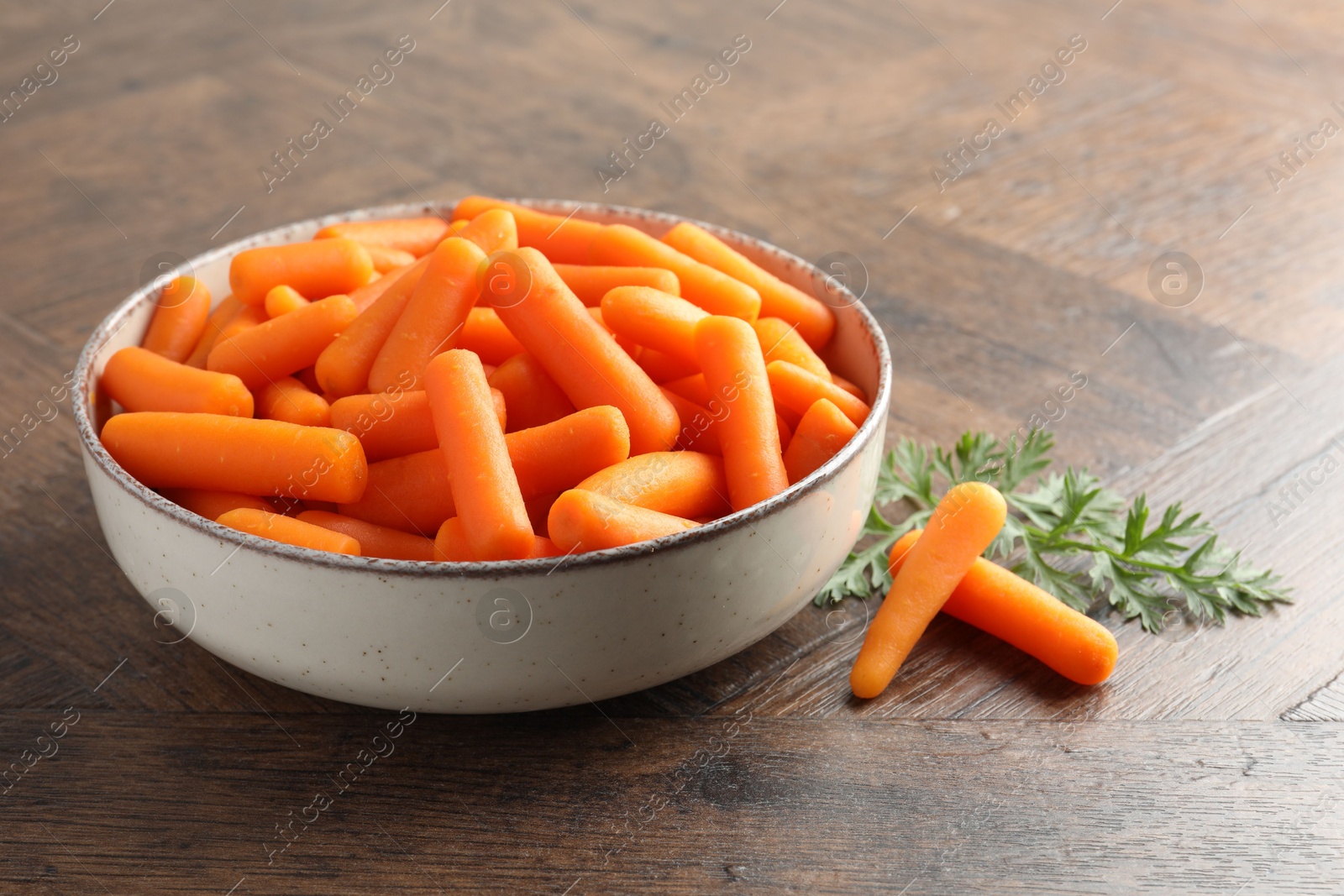 Photo of Baby carrots in bowl and green leaf on wooden table