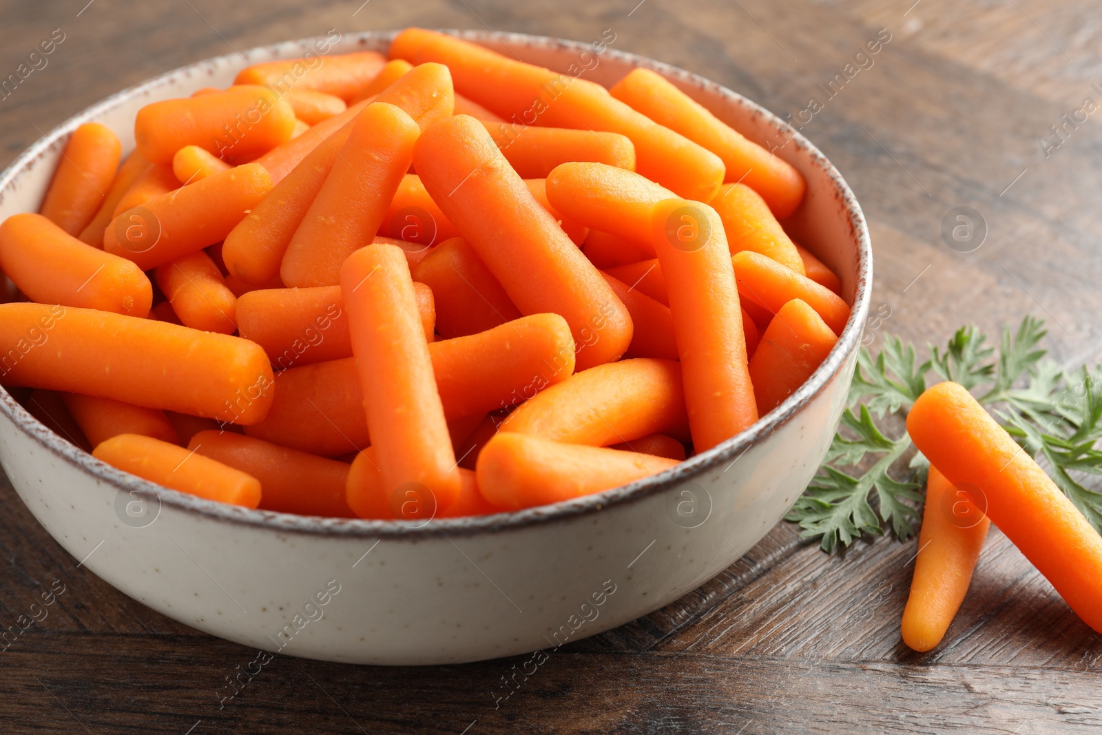 Photo of Baby carrots in bowl and green leaf on wooden table