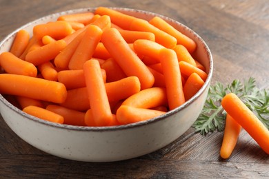 Baby carrots in bowl and green leaf on wooden table