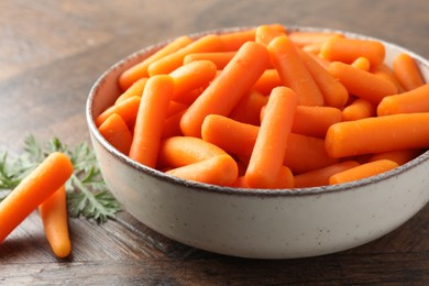 Baby carrots in bowl and green leaf on wooden table