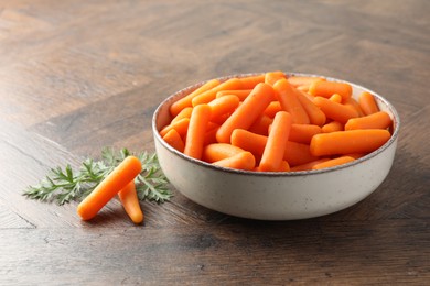 Photo of Baby carrots in bowl and green leaf on wooden table