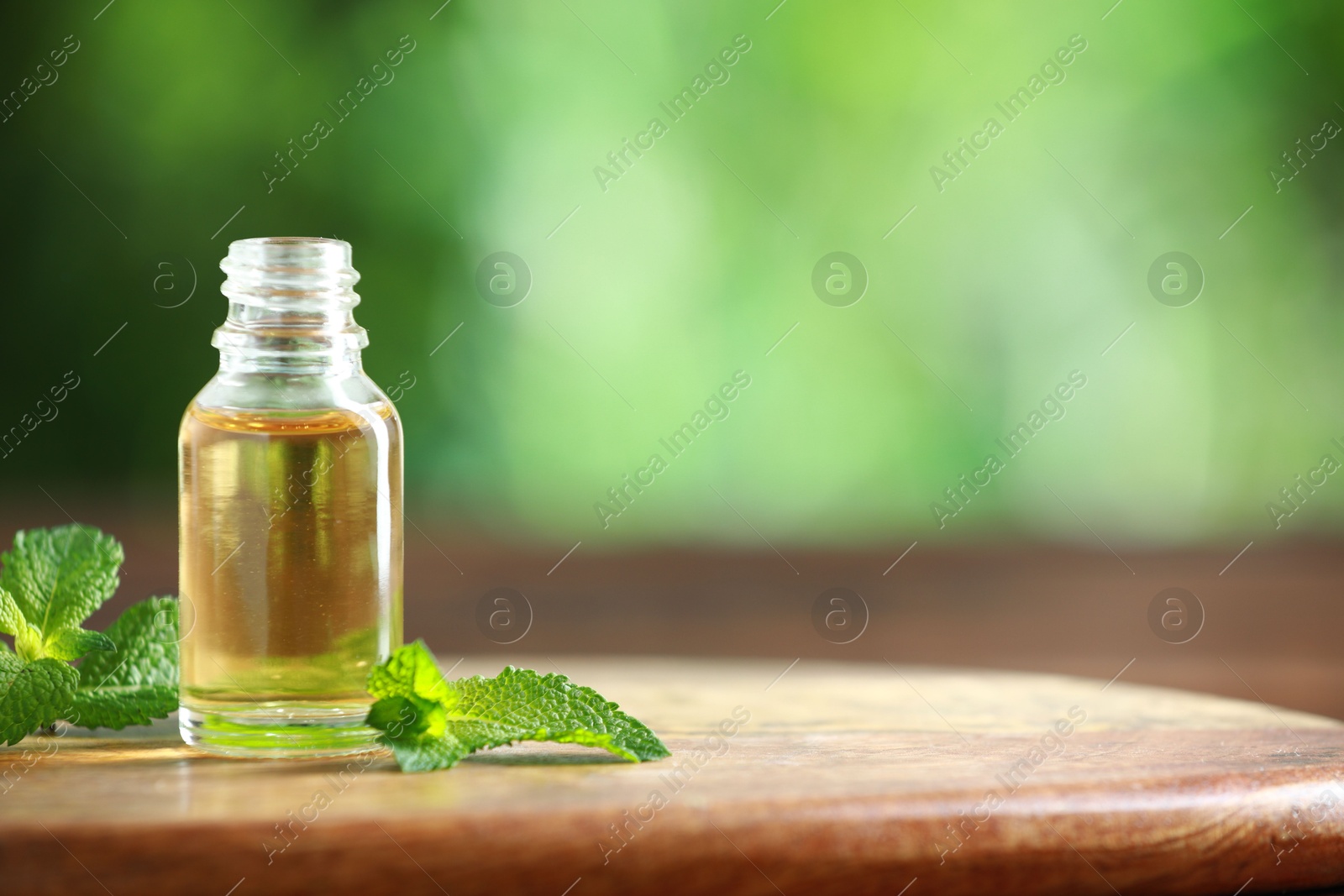 Photo of Bottle of mint essential oil and fresh leaves on wooden table, space for text