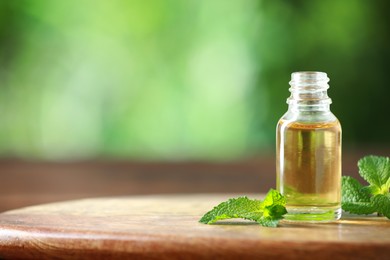 Photo of Bottle of mint essential oil and fresh leaves on wooden table, space for text