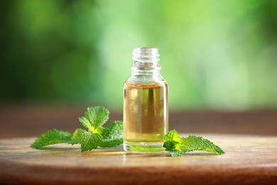 Bottle of mint essential oil and fresh leaves on wooden table