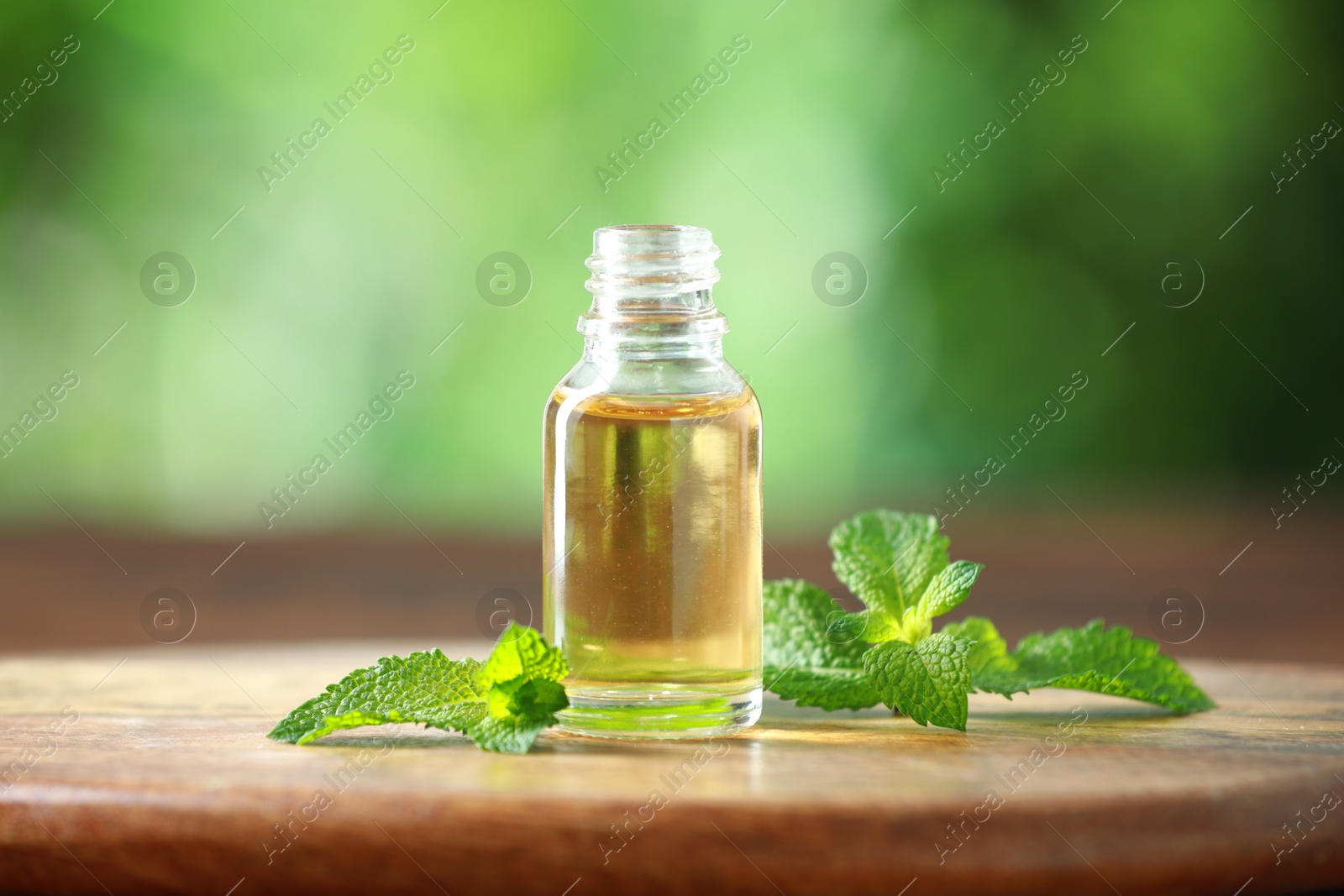 Photo of Bottle of mint essential oil and fresh leaves on wooden table