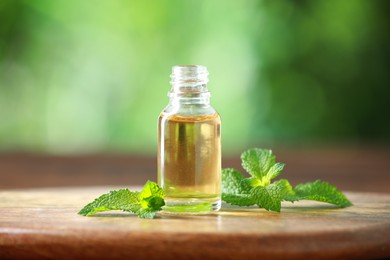 Bottle of mint essential oil and fresh leaves on wooden table