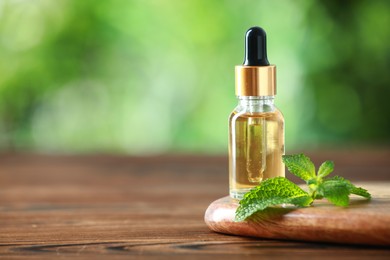 Bottle of mint essential oil and fresh leaves on wooden table, space for text