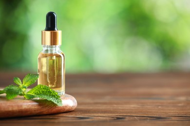 Photo of Bottle of mint essential oil and fresh leaves on wooden table, space for text