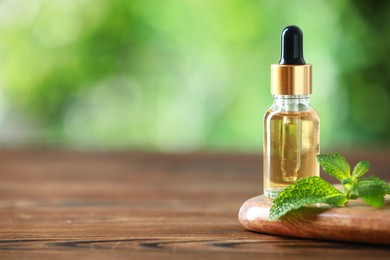 Bottle of mint essential oil and fresh leaves on wooden table, space for text