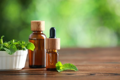 Bottles of mint essential oil and fresh leaves on wooden table, space for text