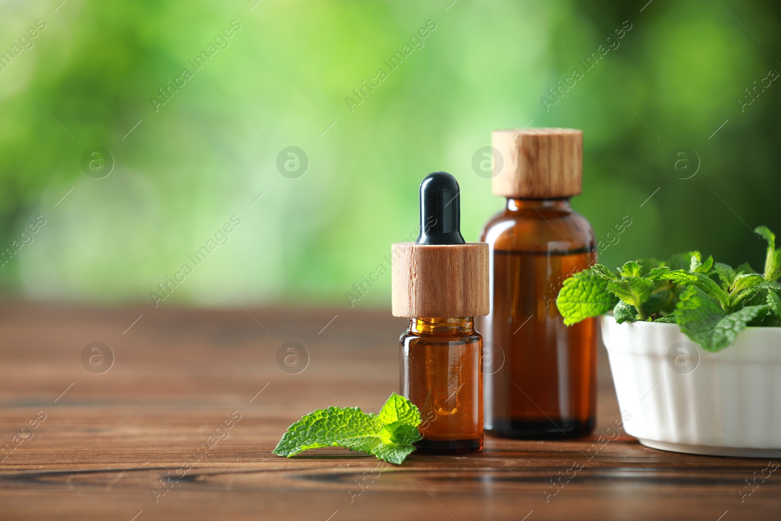 Photo of Bottles of mint essential oil and fresh leaves on wooden table, space for text