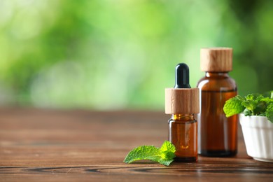 Bottles of mint essential oil and fresh leaves on wooden table, space for text