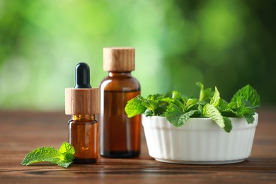 Photo of Bottles of mint essential oil and fresh leaves on wooden table