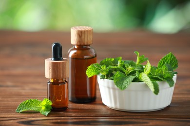 Bottles of mint essential oil and fresh leaves on wooden table