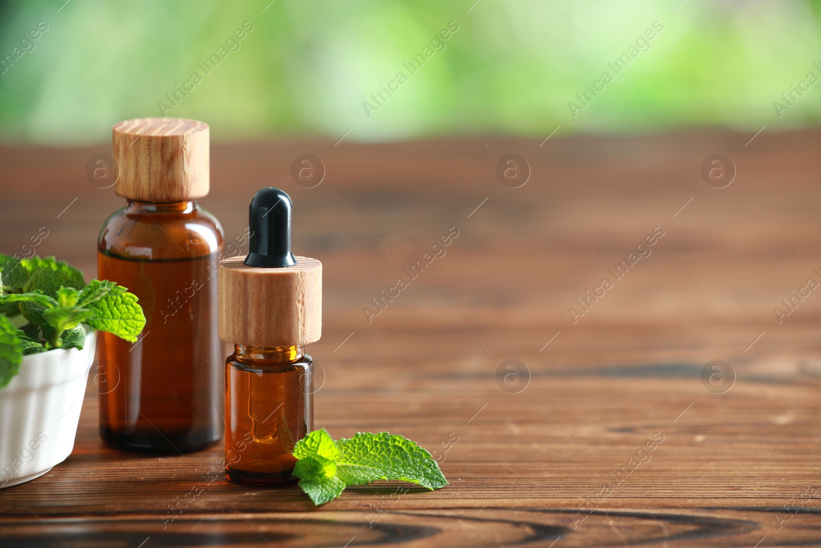 Photo of Bottles of mint essential oil and fresh leaves on wooden table, space for text