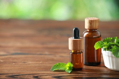 Photo of Bottles of mint essential oil and fresh leaves on wooden table, space for text