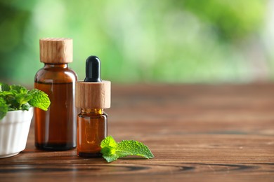 Bottles of mint essential oil and fresh leaves on wooden table, space for text