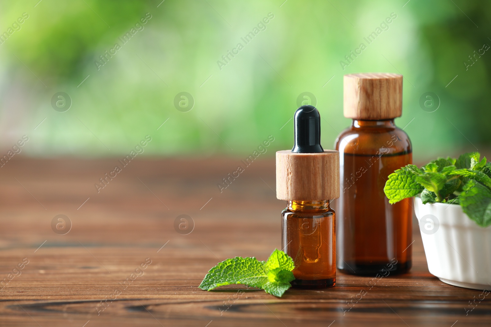 Photo of Bottles of mint essential oil and fresh leaves on wooden table, space for text