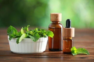 Photo of Bottles of mint essential oil and fresh leaves on wooden table