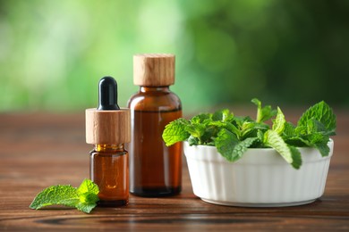 Bottles of mint essential oil and fresh leaves on wooden table