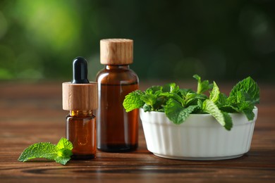 Bottles of mint essential oil and fresh leaves on wooden table