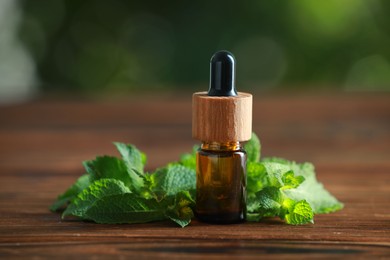 Bottle of mint essential oil and fresh leaves on wooden table