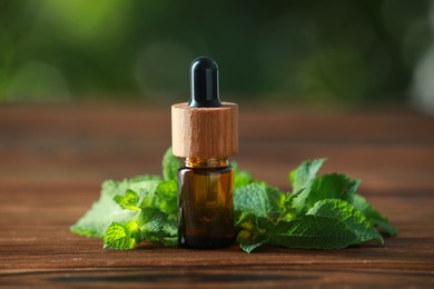 Bottle of mint essential oil and fresh leaves on wooden table