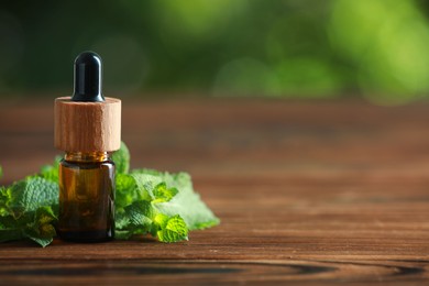 Bottle of mint essential oil and fresh leaves on wooden table, space for text