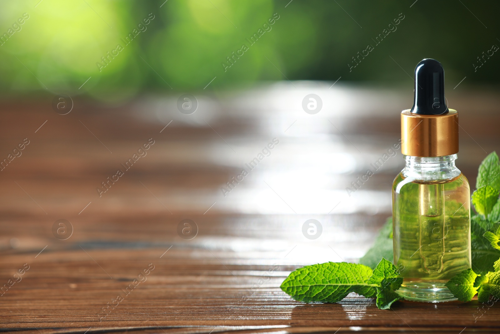 Photo of Bottle of mint essential oil and fresh leaves on wooden table, space for text