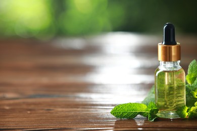 Bottle of mint essential oil and fresh leaves on wooden table, space for text