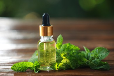 Bottle of mint essential oil and fresh leaves on wooden table