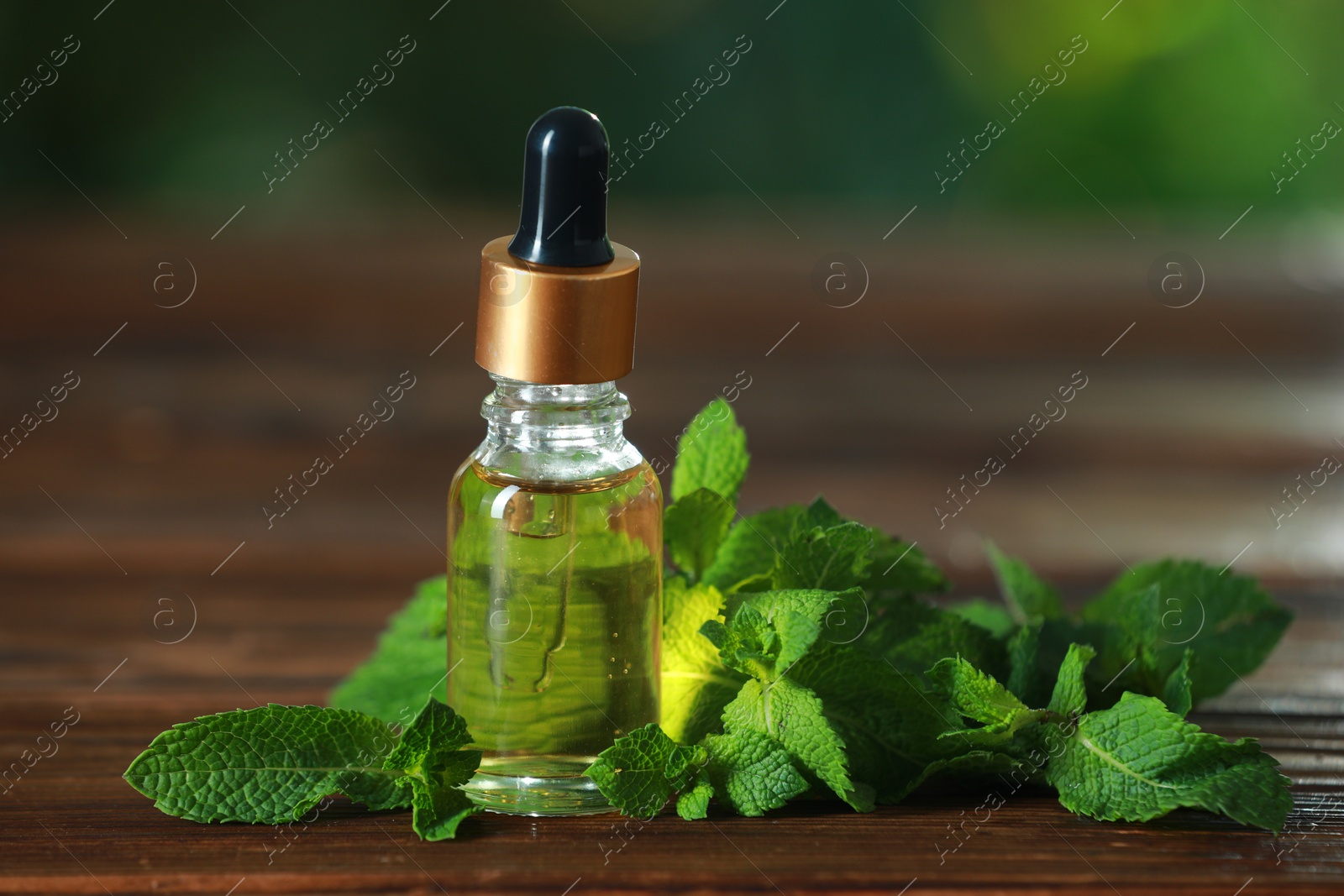 Photo of Bottle of mint essential oil and fresh leaves on wooden table