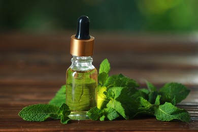 Bottle of mint essential oil and fresh leaves on wooden table