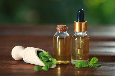 Bottles of mint essential oil and fresh leaves on wooden table