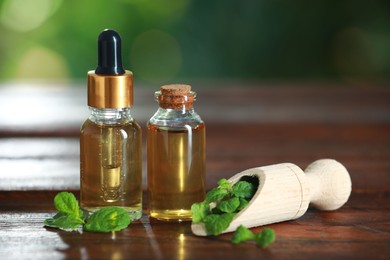 Photo of Bottles of mint essential oil and fresh leaves on wooden table