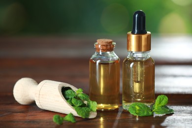 Bottles of mint essential oil and fresh leaves on wooden table