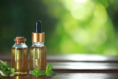 Photo of Bottles of mint essential oil and fresh leaves on wooden table, space for text