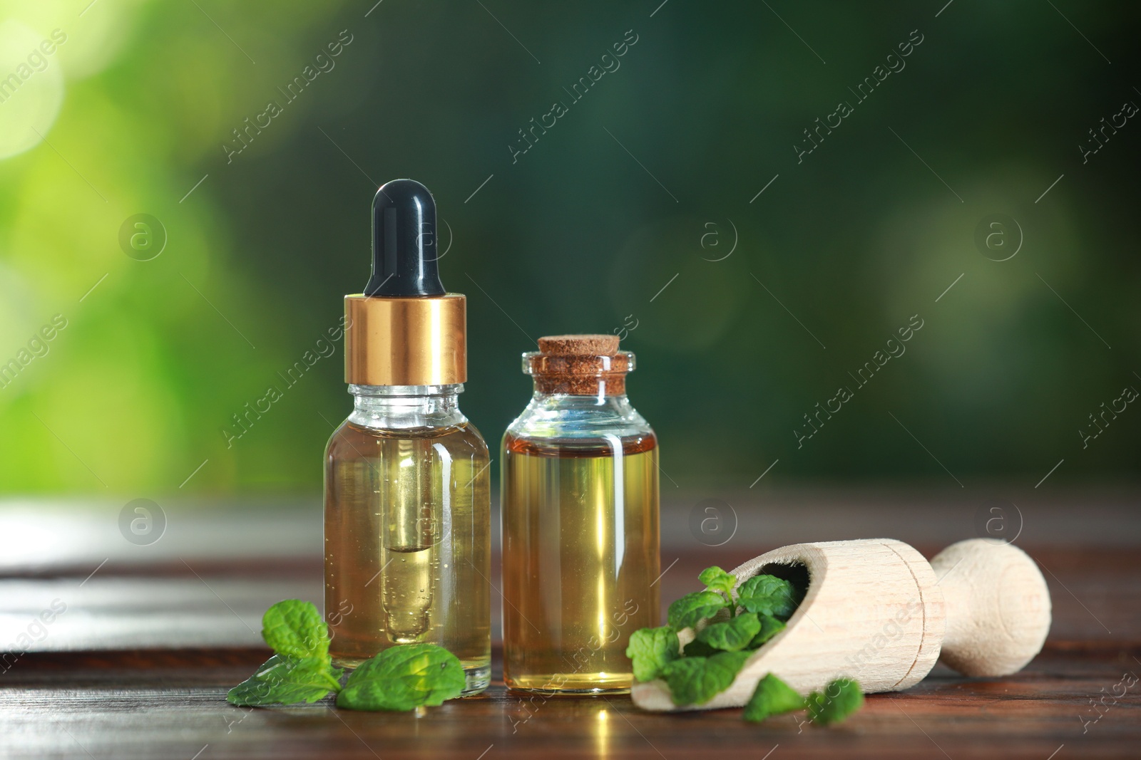 Photo of Bottles of mint essential oil and fresh leaves on wooden table