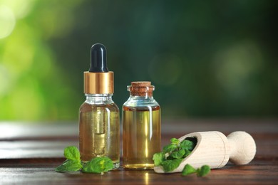 Bottles of mint essential oil and fresh leaves on wooden table