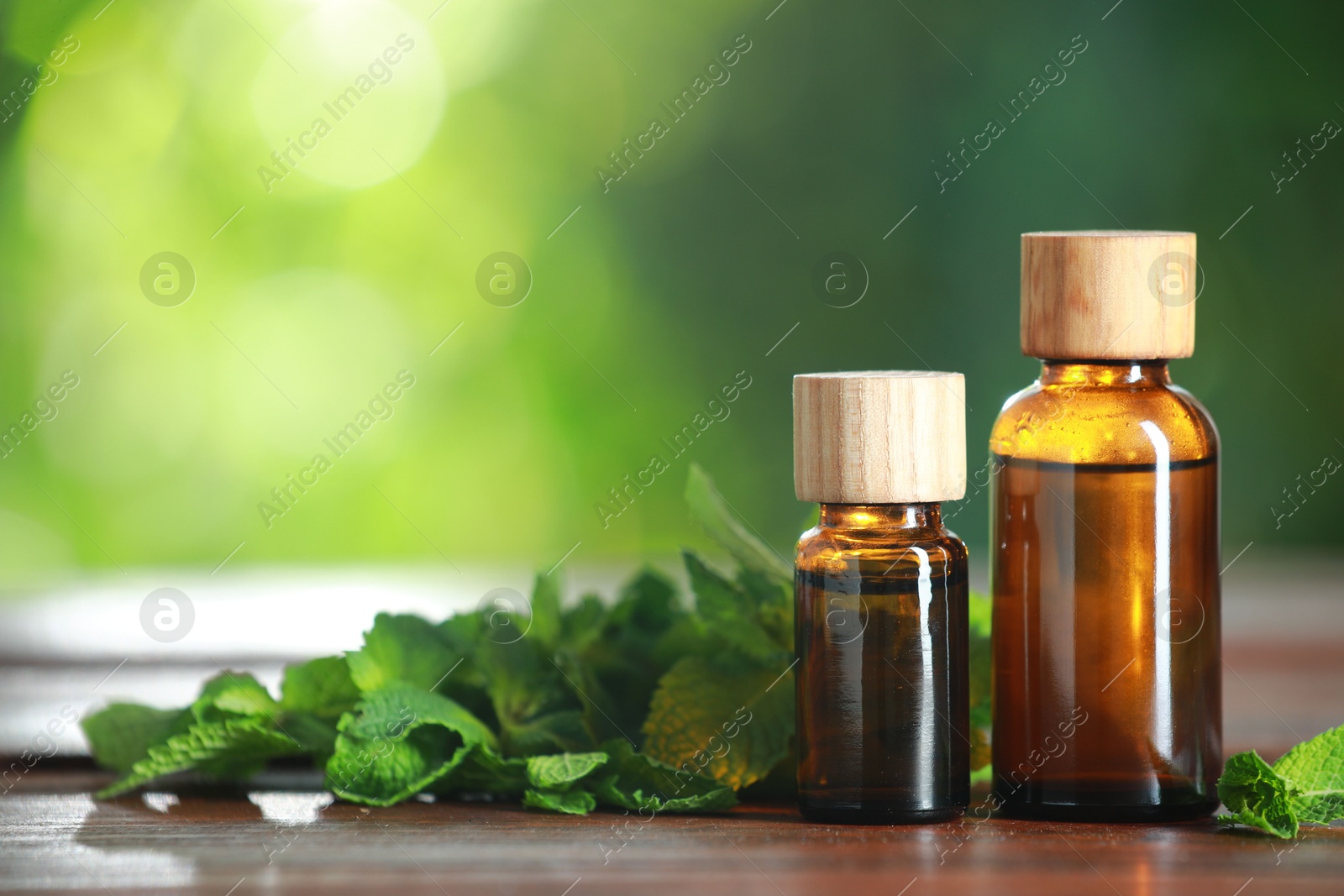 Photo of Bottles of mint essential oil and fresh leaves on wooden table, space for text