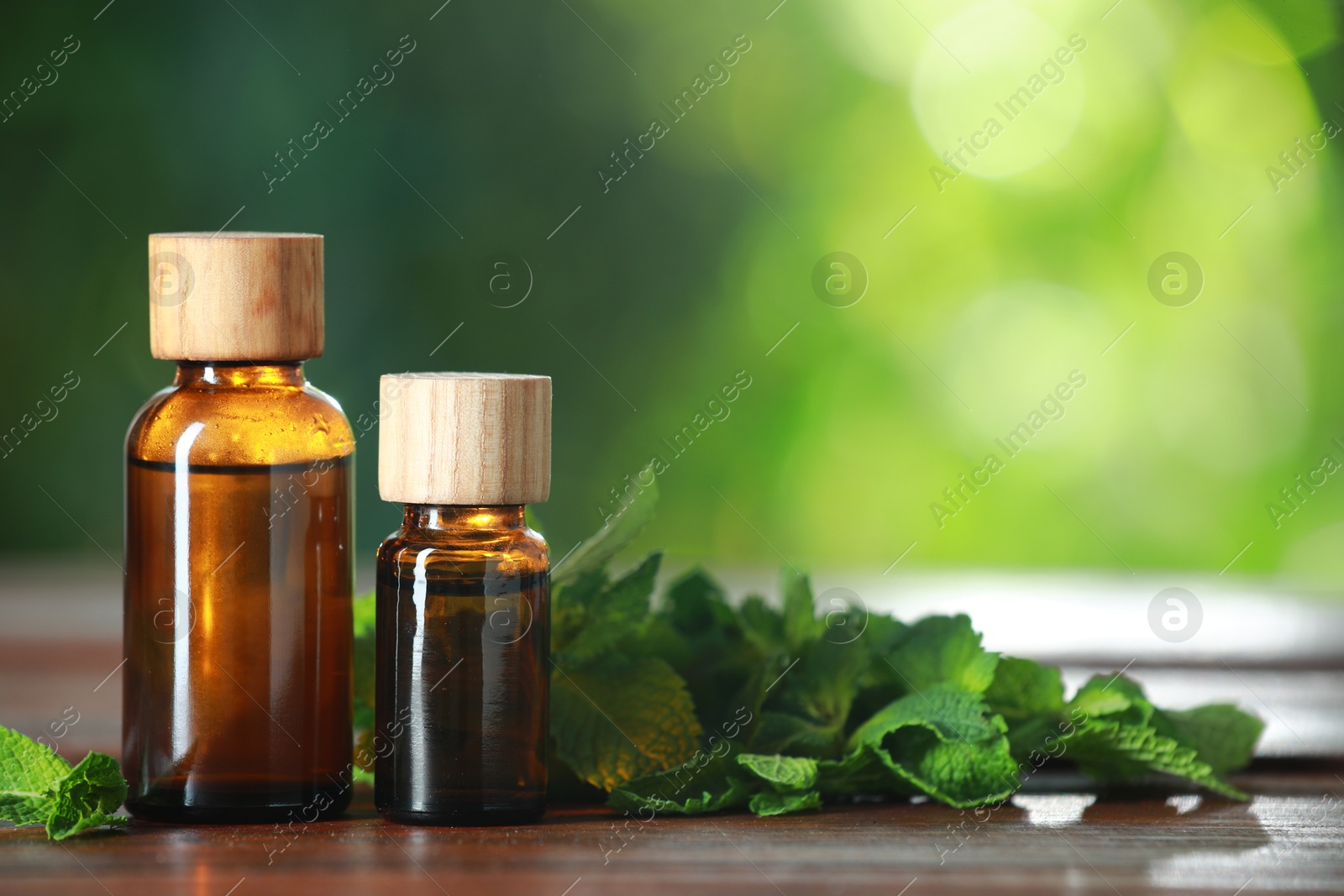 Photo of Bottles of mint essential oil and fresh leaves on wooden table, space for text