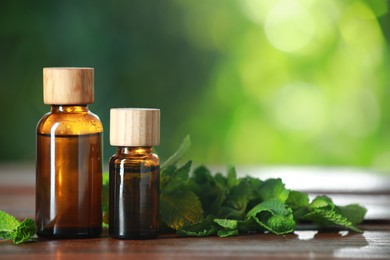 Bottles of mint essential oil and fresh leaves on wooden table, space for text